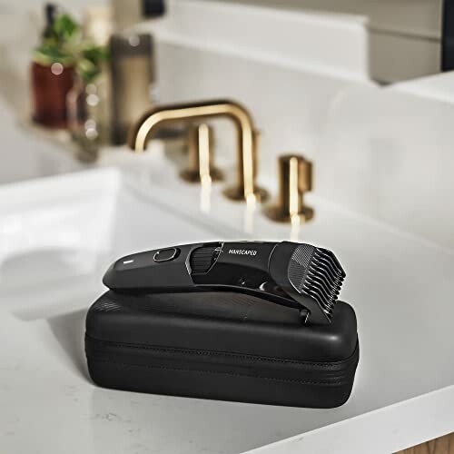 Electric trimmer on a black case beside a sink with gold faucet.