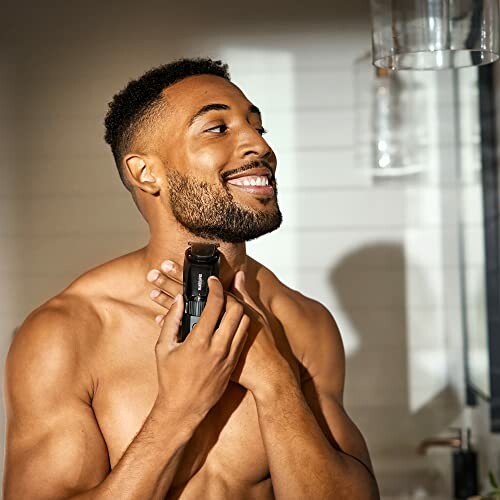 Man trimming beard with electric trimmer in bathroom.